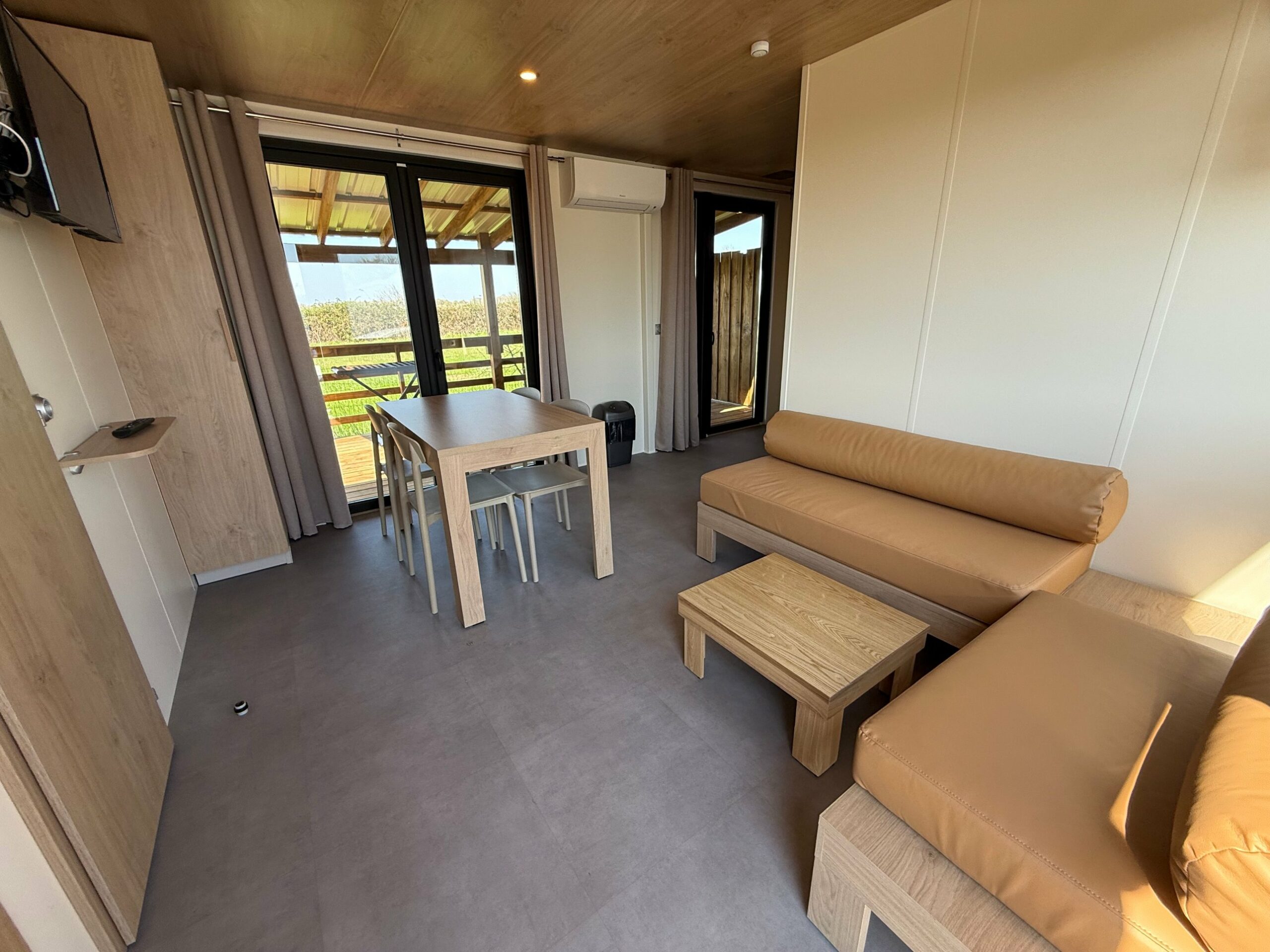 Séjour climatisé d’un mobil-home avec baie vitrée sur la terrasse, au camping Crin Blanc